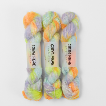 Three labelled hanks of 600 Volts Melted Baby Suri 25g yarn in yellow and orange with green and lilac.