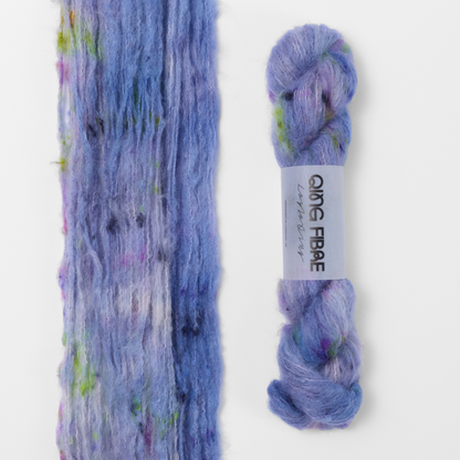 Moon Goddess Melted Baby Suri 25g: lavender with pink and green accents yarn, shown loose beside a labelled hank.