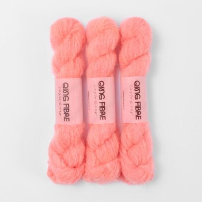 Three labelled hanks of Shrimp Melted Baby Suri 25g yarn in coral orange.