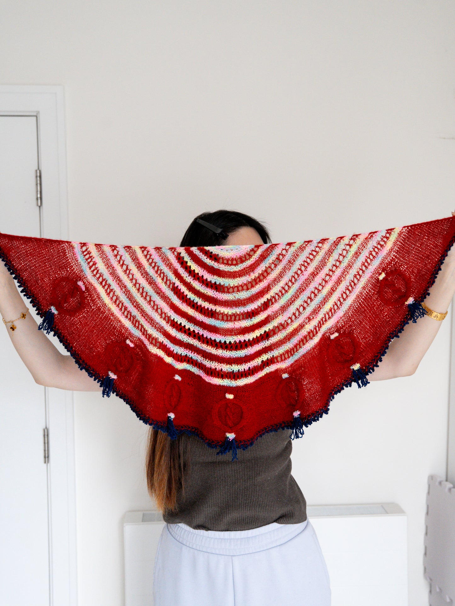 Person wearing a red and white patterned shawl with blue tassels.