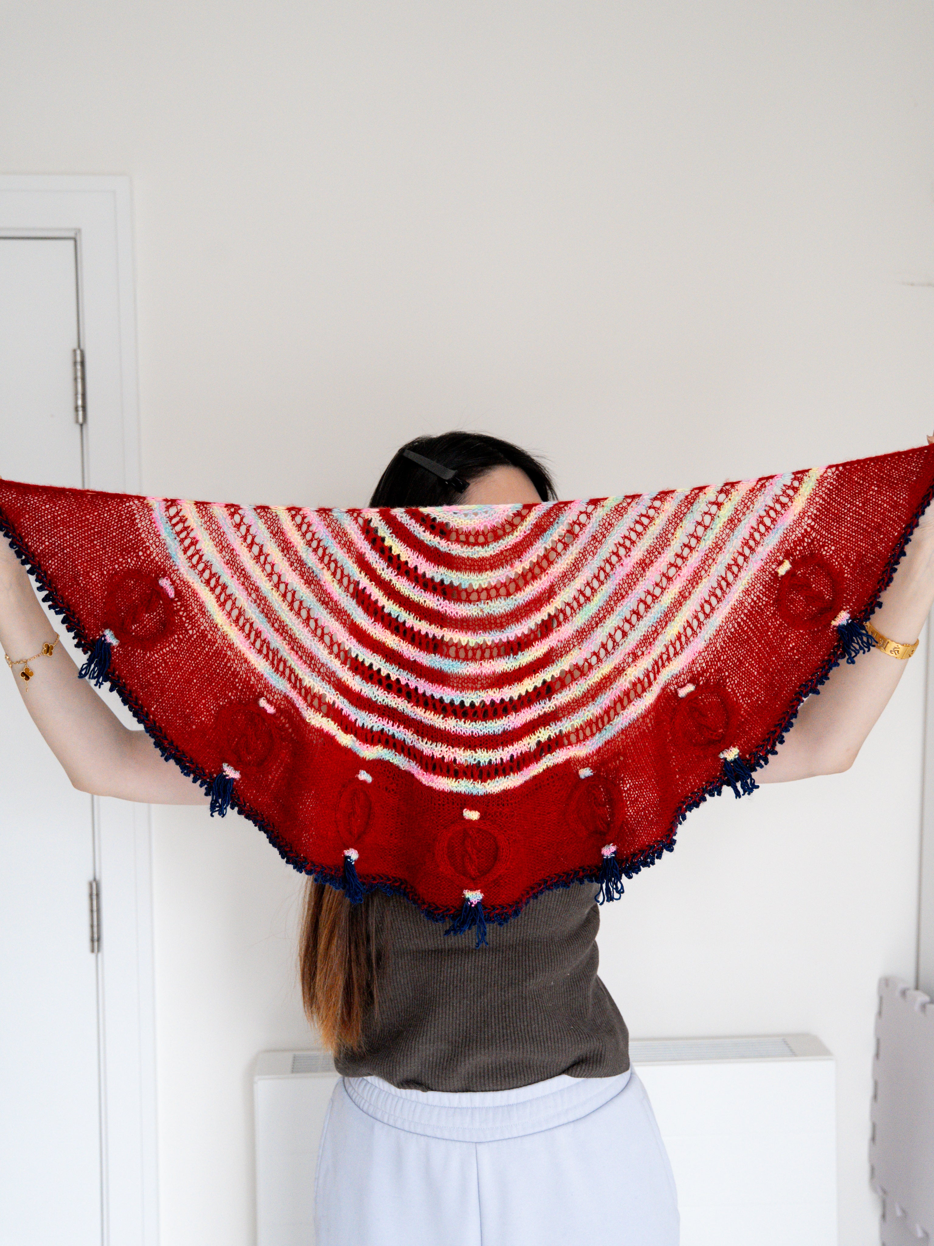 Person wearing a red and white patterned shawl with blue tassels.