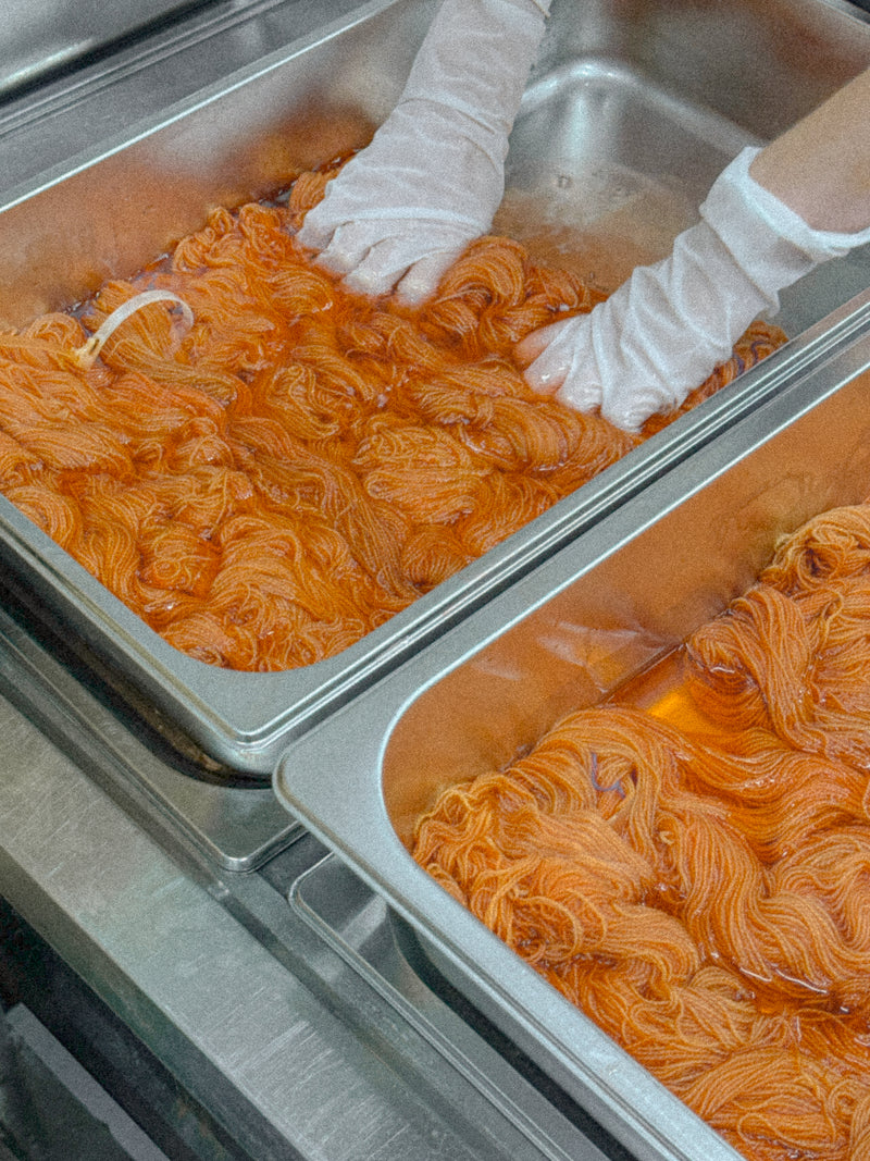Hand-dyeing yarn in a London studio — skeins immersed in a warm amber dye bath by Qing Fibre