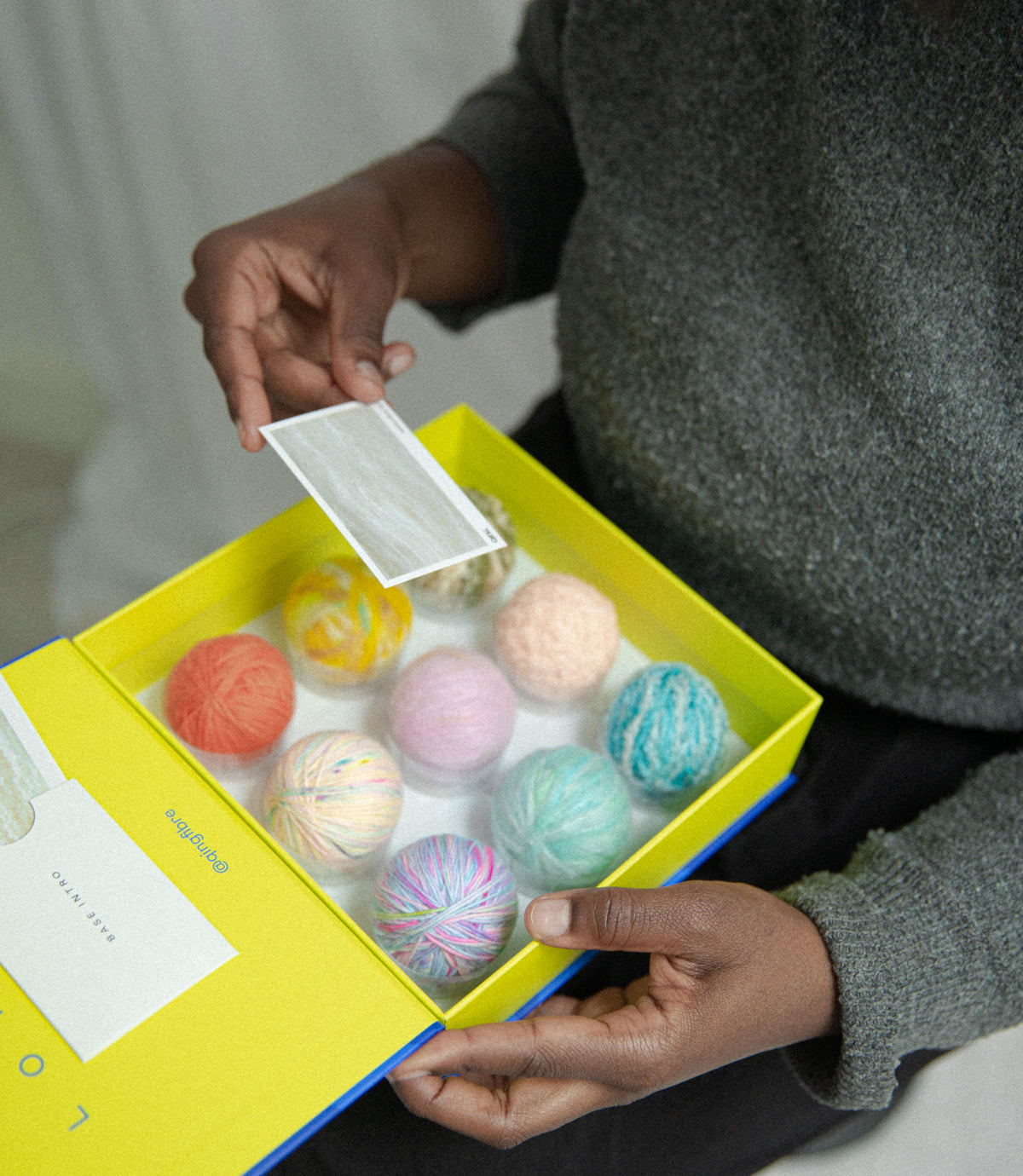 Hands unboxing the Qing Fibre Taster Box, revealing 9 hand-dyed mini yarn balls and colour cards