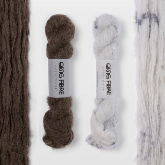 Soot and Platinum Melted Baby Suri 25g yarn, with two twisted skeins between the open skeins on a grey background.