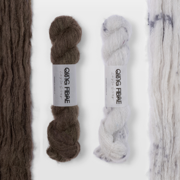 Soot and Platinum Melted Baby Suri 25g yarn, with two twisted skeins between the open skeins on a grey background.